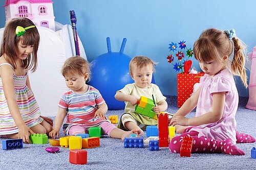 Four toddlers playing with plastic bricks.