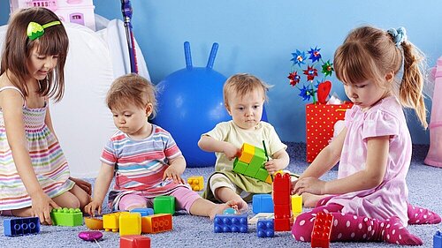 Four toddlers playing with plastic bricks.